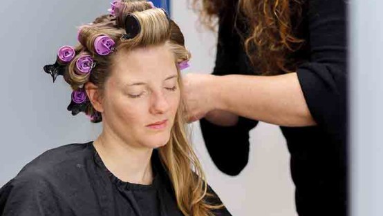 Schauspielern mit Lockenwicklern und Maskenbildnerin.