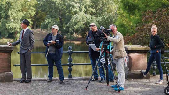 Kamerateam und Schauspieler beim Außendreh an einem Park.
