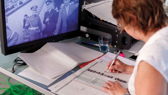 Regie macht Notizen im Drehbuch, vor ihr ein Monitor mit historischem Foto.