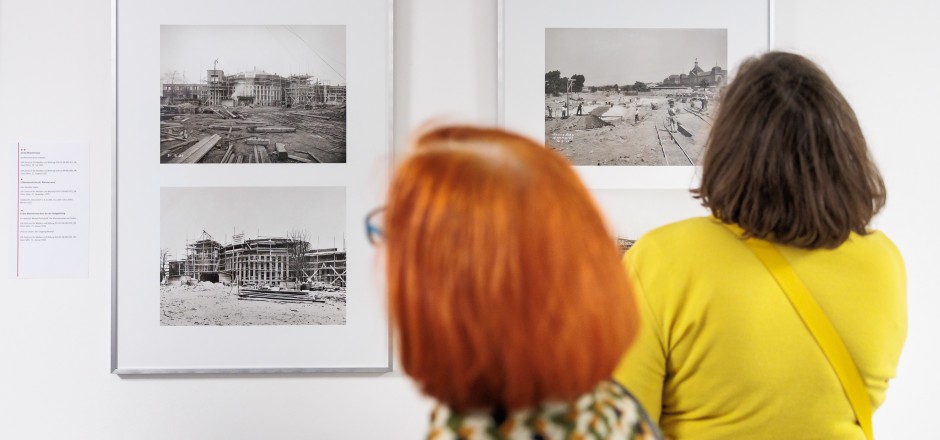 Zwei Frauen schauen sich Fotos an, die in Bilderrahmen an der Wand hängen.