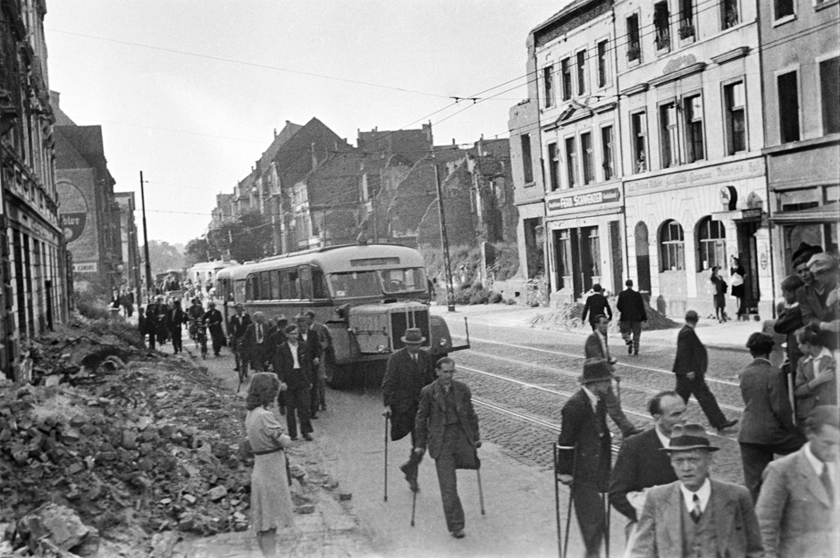 Passanten auf einer Straße, neben der Trümmer liegen