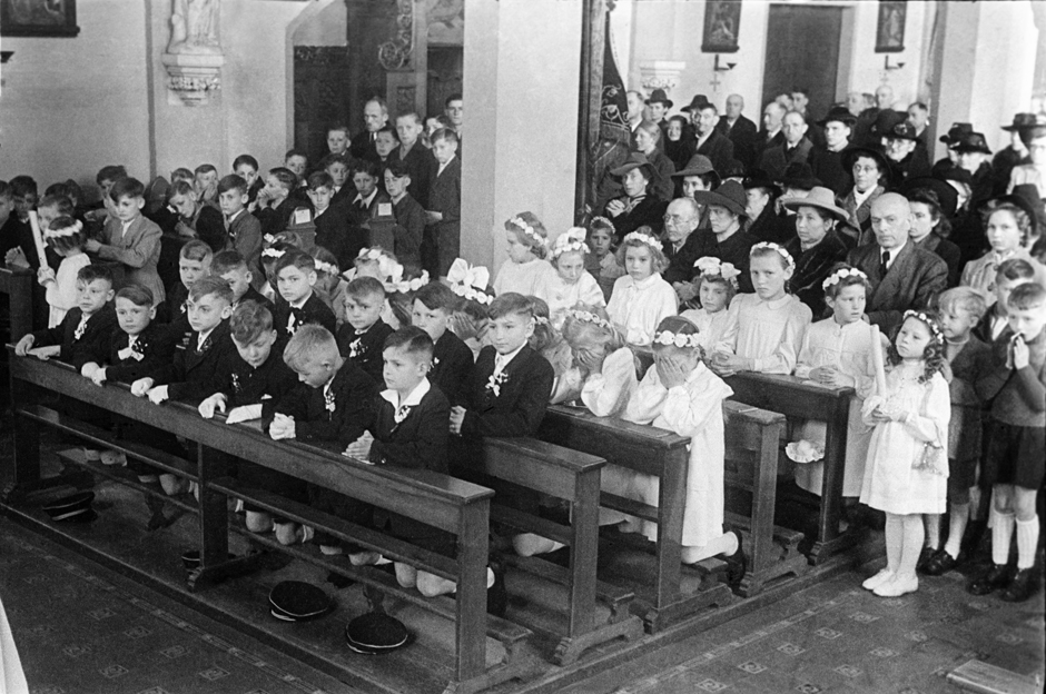 Kommunionkinder knien in den Kirchenbänken