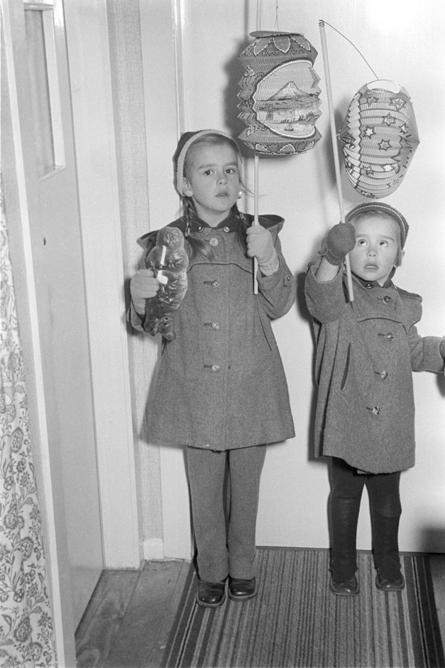 Zwei Kinder stehen mit Laternen in einer Wohnung.