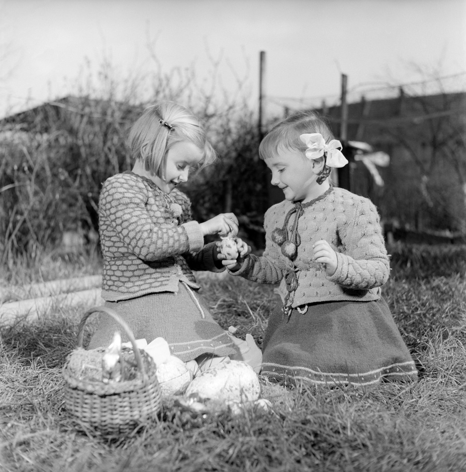 Zwei Mädchen sitzen mit Ostereiern im Garten.