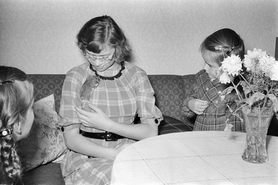 Eine Frau und zwei Kinder sitzen mit einem Hamster auf einem Sofa.