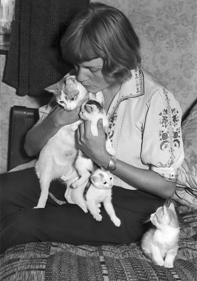 Eine Frau sitzt mit mehreren Katzen auf dem Sofa.