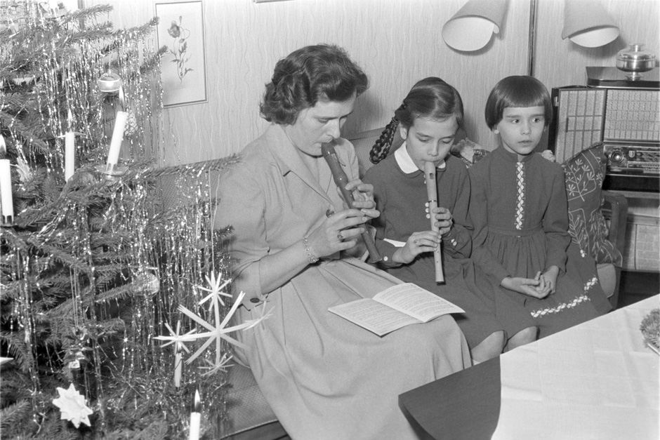 Eine Frau sitzt mit zwei Mädchen auf dem Sofa und spielt Flöte.