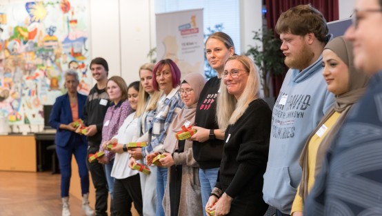 Die MEDITA-Kitas stehen in einer Reihe vor der Bühne aufgestellt und lachen dankend über die Dankesgeschenke in ihren Händen.
