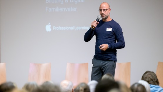 Der Fachreferent Martin Mucha steht mit Mikro auf der Bühne vor dem Publikum des Fachtags. 