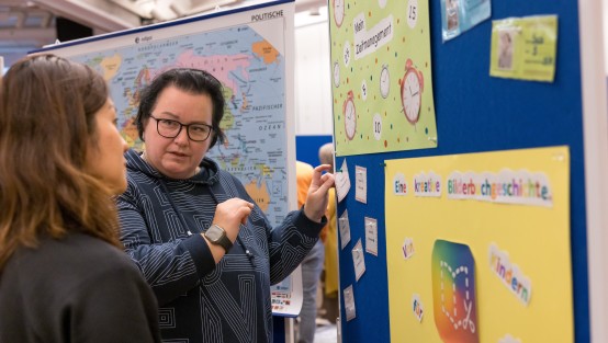 Eine Kita-Fachkraft im Gespräch mit einer MEDITA-Kita-Fachkraft vor einer Stellwand zum Thema Medienzeit-Management der Kinder.