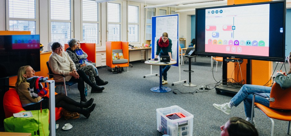 Auf einem Tisch stehen eine Toniebox mit einer Benjamin Blümchen-Figur und ein Tablet mit der passenden App. Eine Person, die von hinten zu sehen ist, berührt den Bildschirm.