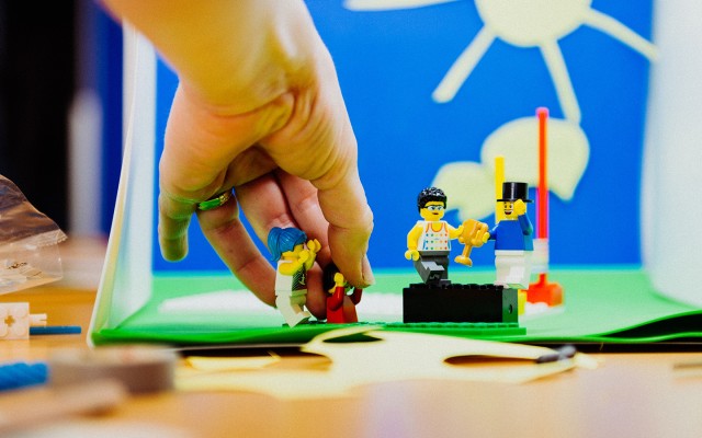 Eine Hand richtet Lego-Männchen zurecht in einem Stop-Motion-Set mit selbst gebasteltem Hintergrund.