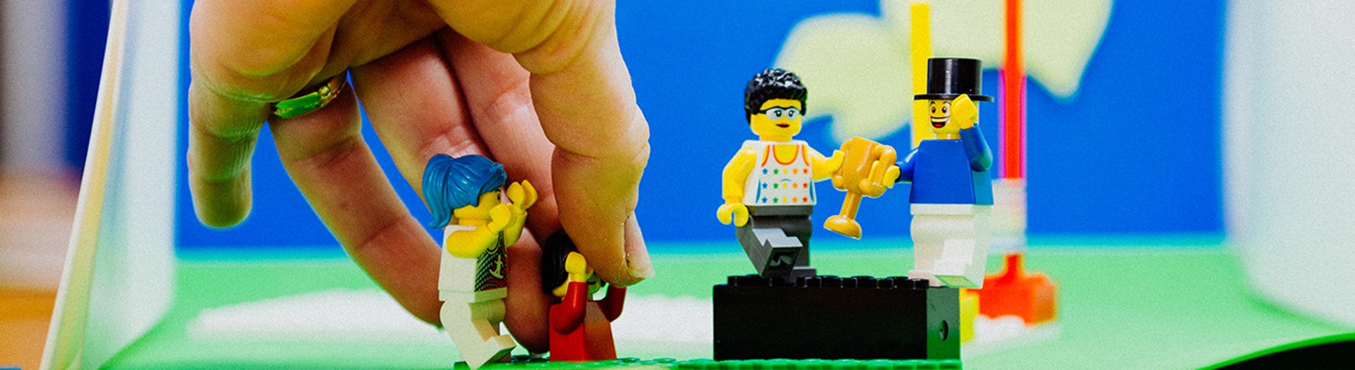 Eine Hand richtet Lego-Männchen zurecht in einem Stop-Motion-Set mit selbst gebasteltem Hintergrund.