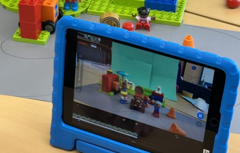 Im Vordergrund ein Tablet, das Lego Figuren und eine Kulisse im Hintergrund aufnimmt.