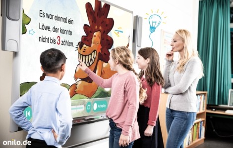 Eine Lehrer*in steht mit Kindern vor einer Boardstory. 