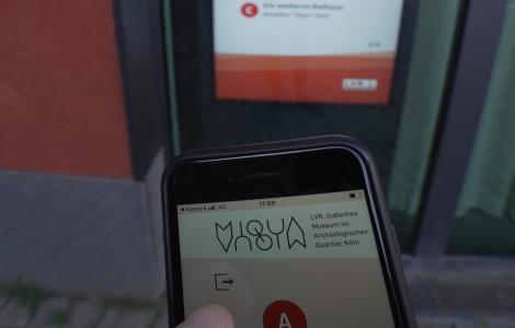 Eine Hand hält ein Handy vor einem Bildschirm.