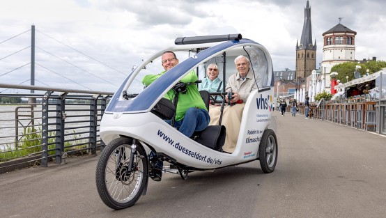 Ein Fahrer und zwei Passagiere in der Fahrrad-Rikscha der VHS Düsseldorf