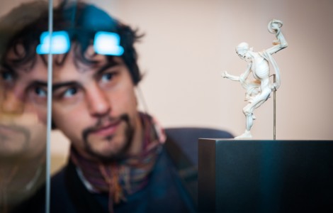 Ein Mann betrachtet eine kleine Skelettfigur - den Tod. Der Mann spiegelt sich in der Vitrine.