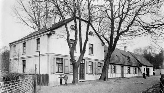 Zwei Kinder vor Dorfhaus mit Zwei mächtigen Bäumen