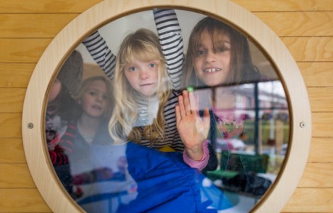 4 Schulmädchen schauen durch ein rundes Fenster.