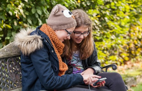 Zwei Mädchen sitzen auf einer Bank und schauen auf ihr Handy.