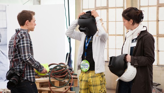 Foto: Julia Reschucha/LVR-ZMB, 2013 Junger Mann setzt sich einen Schweißerhelm auf, beobachtet von einem Fotografen und einer Frau