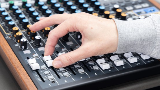 Eine Hand betätigt einen Regler an einem Audio Panel.