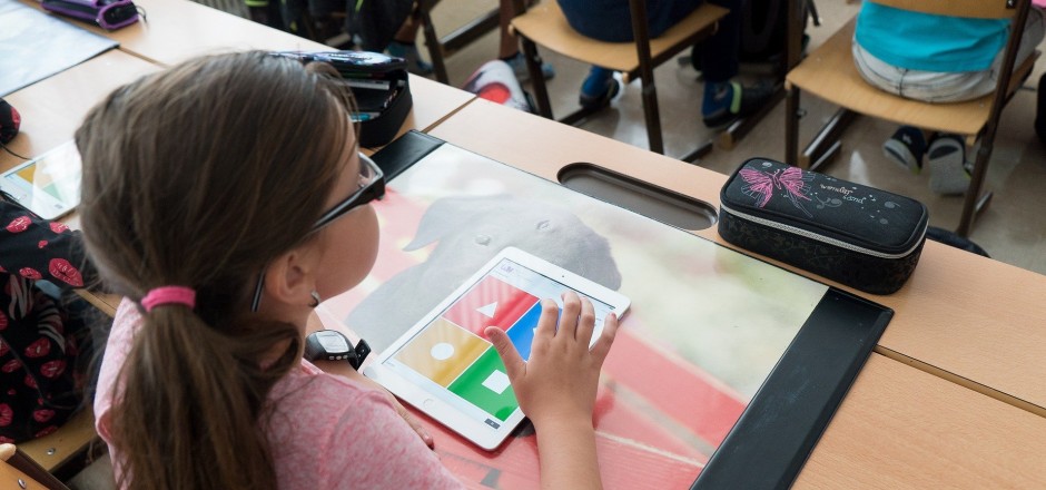 Mädchen sitzt am Schreibtisch, auf dem ein Tablet liegt