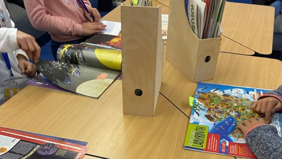 Lesezeit: Auf dem Tisch liegen aufgeschlagene Zeitschriften, die gerade gelesen werden. In der Mitte des Tischs stehen Ordner mit weiteren Zeitschriften. 