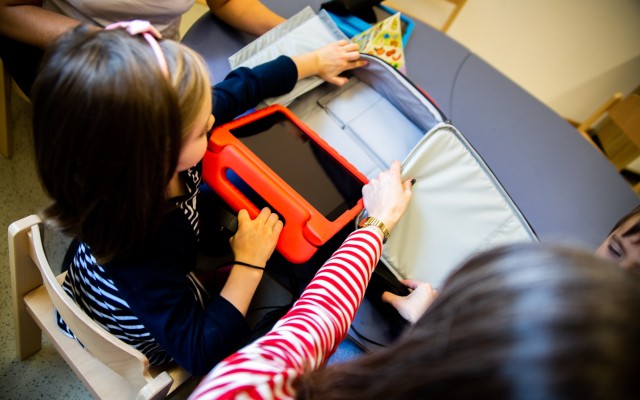 Ein Kind zieht ein Tablet in orangener Schutzhülle aus einem Rucksack